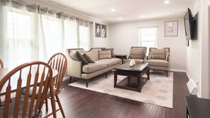 A living room with a sofa, armchairs, a coffee table, wooden chairs, a TV, and a dining table. - Chic Lake Geneva Apartment in Desirable Location! (Lake Geneva)