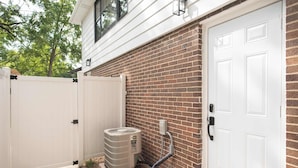 A residential exterior with a brick wall, a white door, and an air conditioning unit. - Chic Lake Geneva Apartment in Desirable Location! (Lake Geneva)