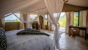 A bedroom with a canopy bed, a desk, and a view of the outdoors. - Cape Vulture Lodge (Hoedspruit)