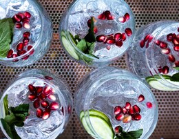 Cuatro vasos de una bebida con hielo, semillas de granada y hojas de menta.