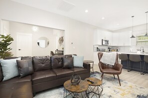 A modern living room with a brown leather sofa, a round coffee table, and a dining area with a bar. - Downtown Modern Living! (Concord)