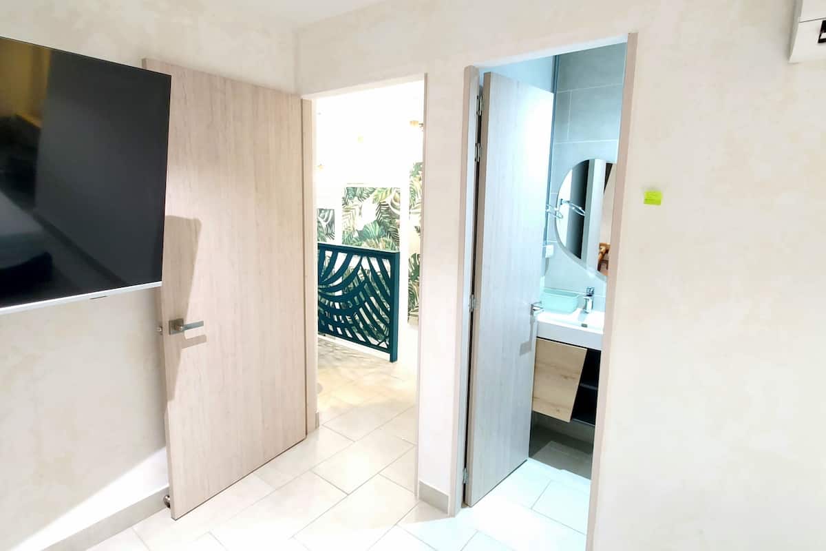 A modern apartment with a TV in a wooden cabinet, a bathroom with a sink and mirror, and a view of the outside.