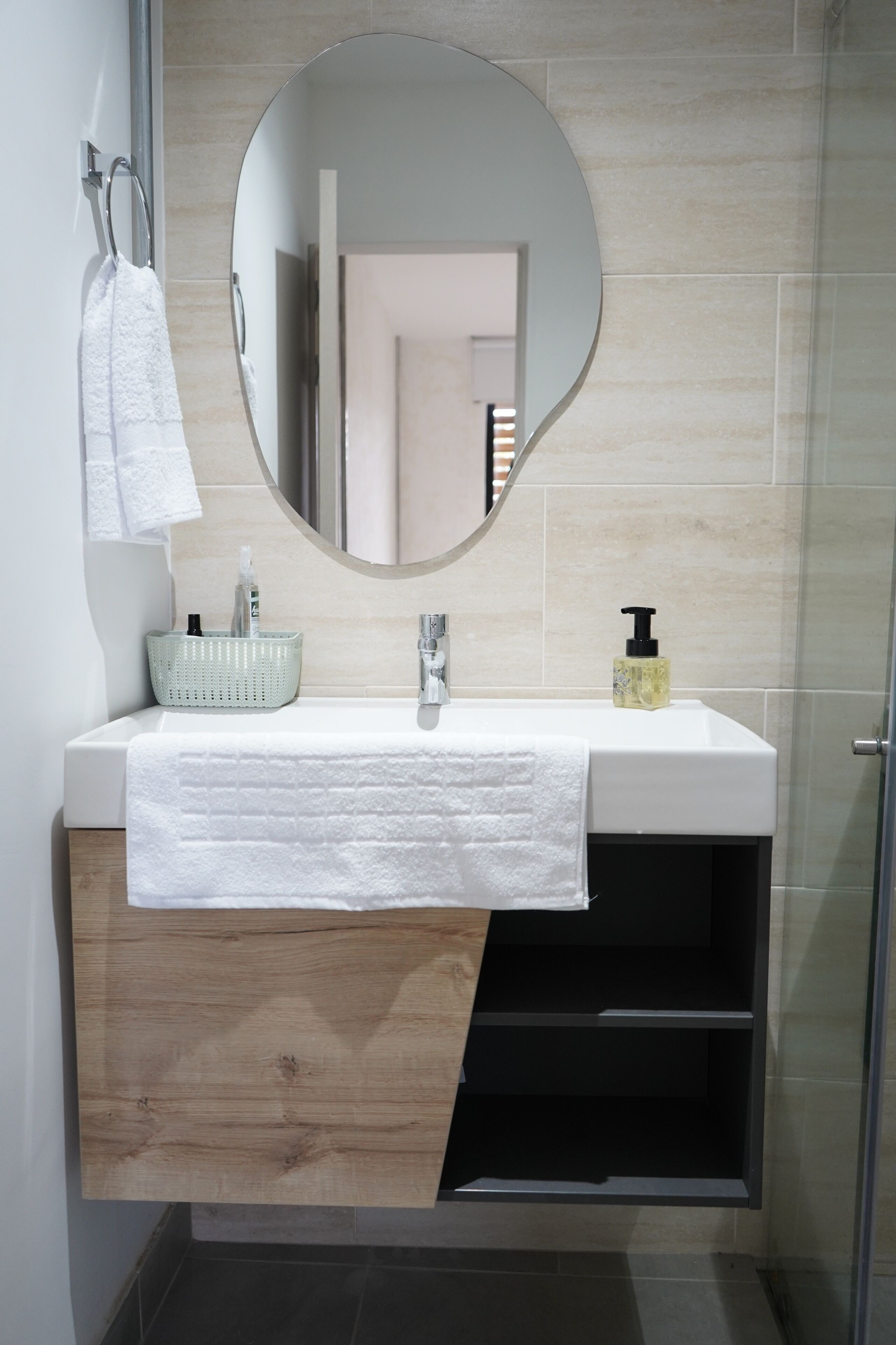 A modern bathroom with a white sink, a round mirror, a towel hanging on a hook, and a soap dispenser.