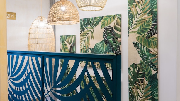Un pasillo con luces decorativas colgantes, un separador azul decorativo y detalles en la pared con estampado de hojas tropicales.