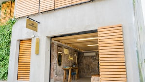 Un edificio moderno con entrada de listones de madera, un letrero que dice 'ZENTRICO' y un interior visible con una mesa y sillas.