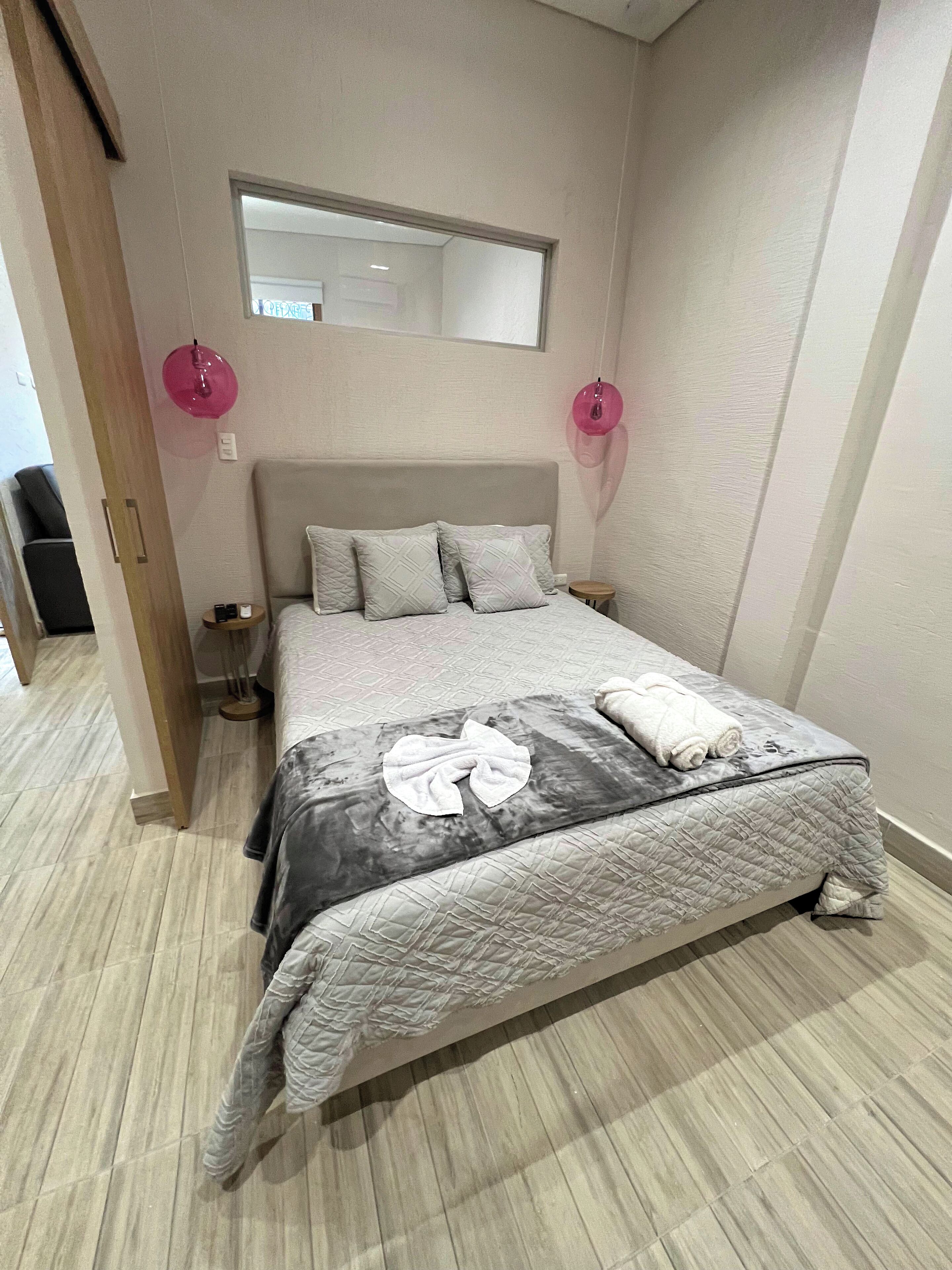 Una cama bien hecha con cubrecama acolchado, dos lámparas de noche y un espejo sobre la cama.