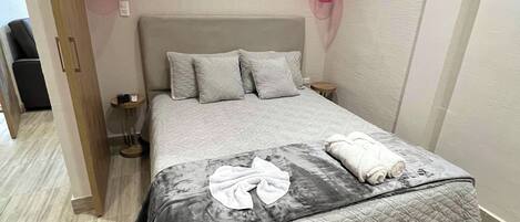 Una cama bien hecha con cubrecama acolchado, dos lámparas de noche y un espejo sobre la cama.
