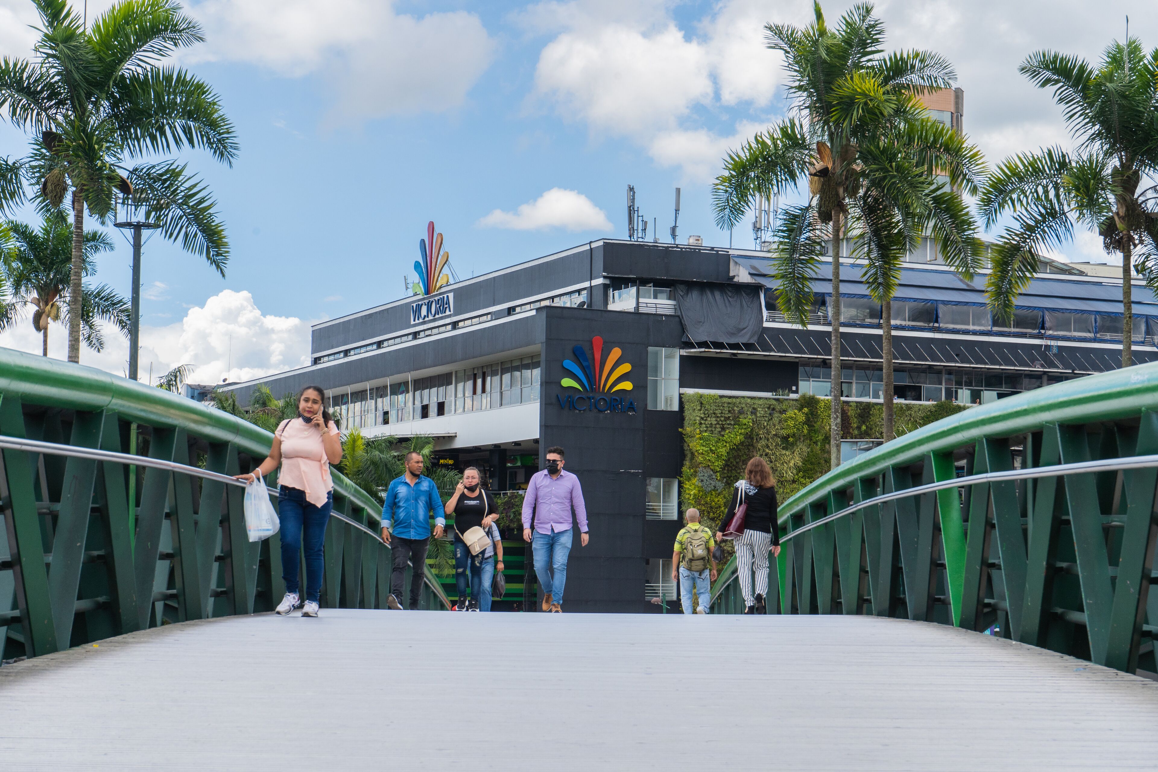 Un puente peatonal de diseño moderno, con un pasillo curvo y barandillas verdes.