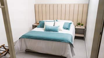 Una cama bien hecha con un cabecero, una mesita de noche con una planta y un taburete pequeño.