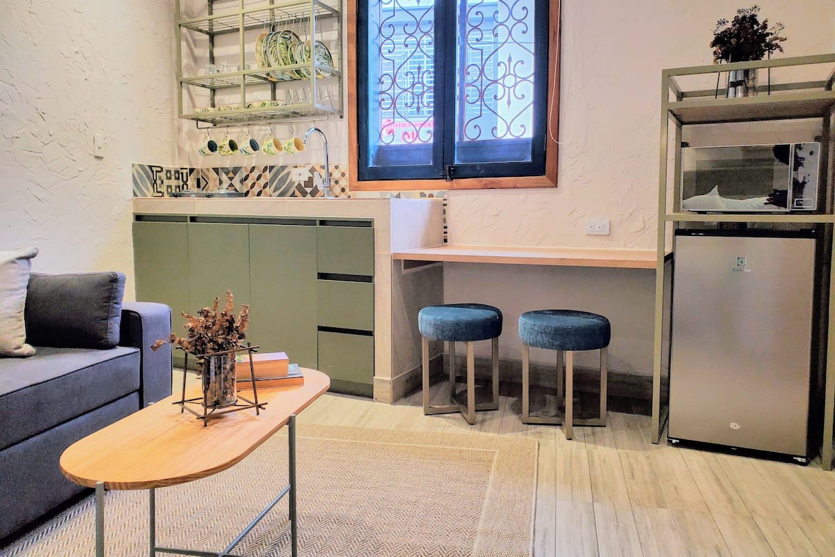 A compact kitchen with a built-in oven, a dining area with stools, and a small seating area with a sofa.