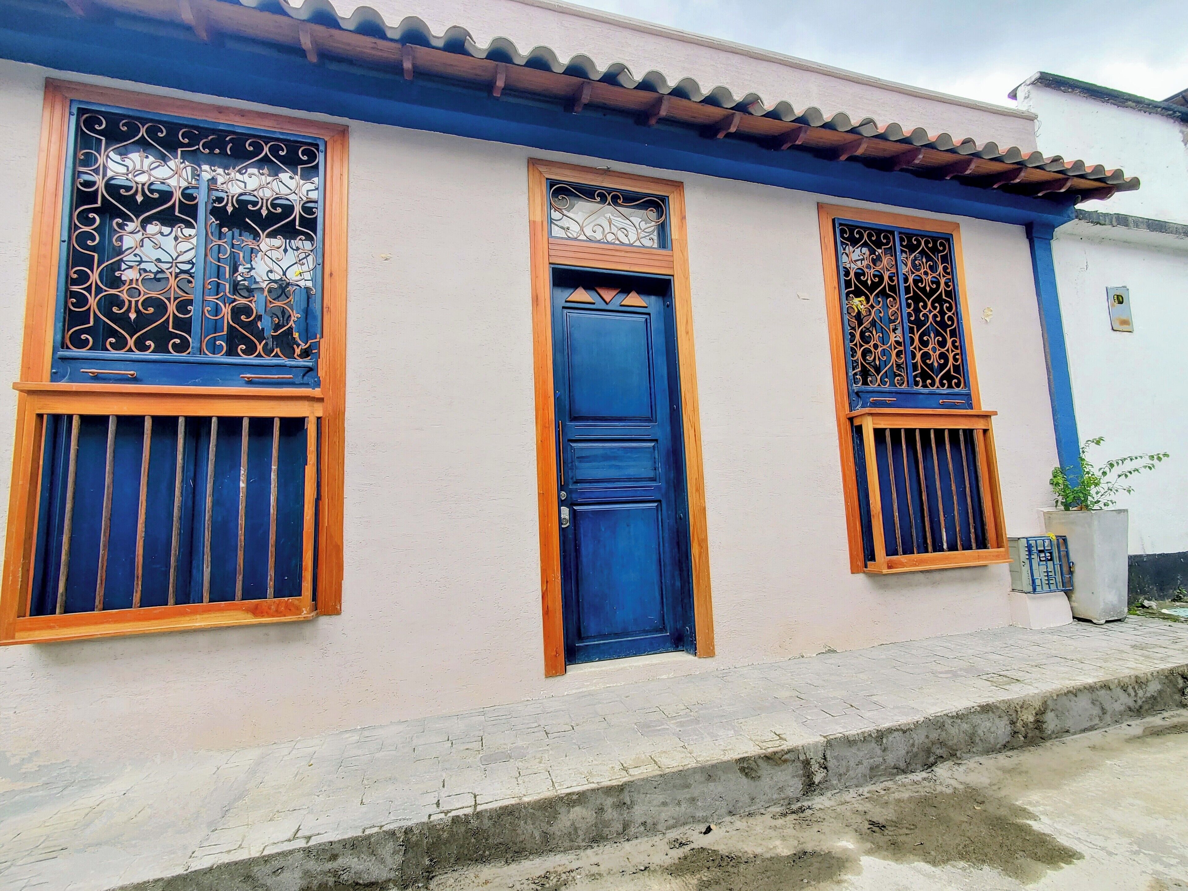 A building with a blue door, two windows with decorative metal grilles, and a tiled roof.