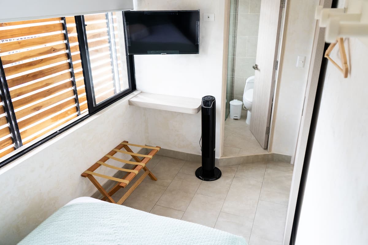A small, modern bathroom with a toilet, a sink, a shower area, and a window with blinds.