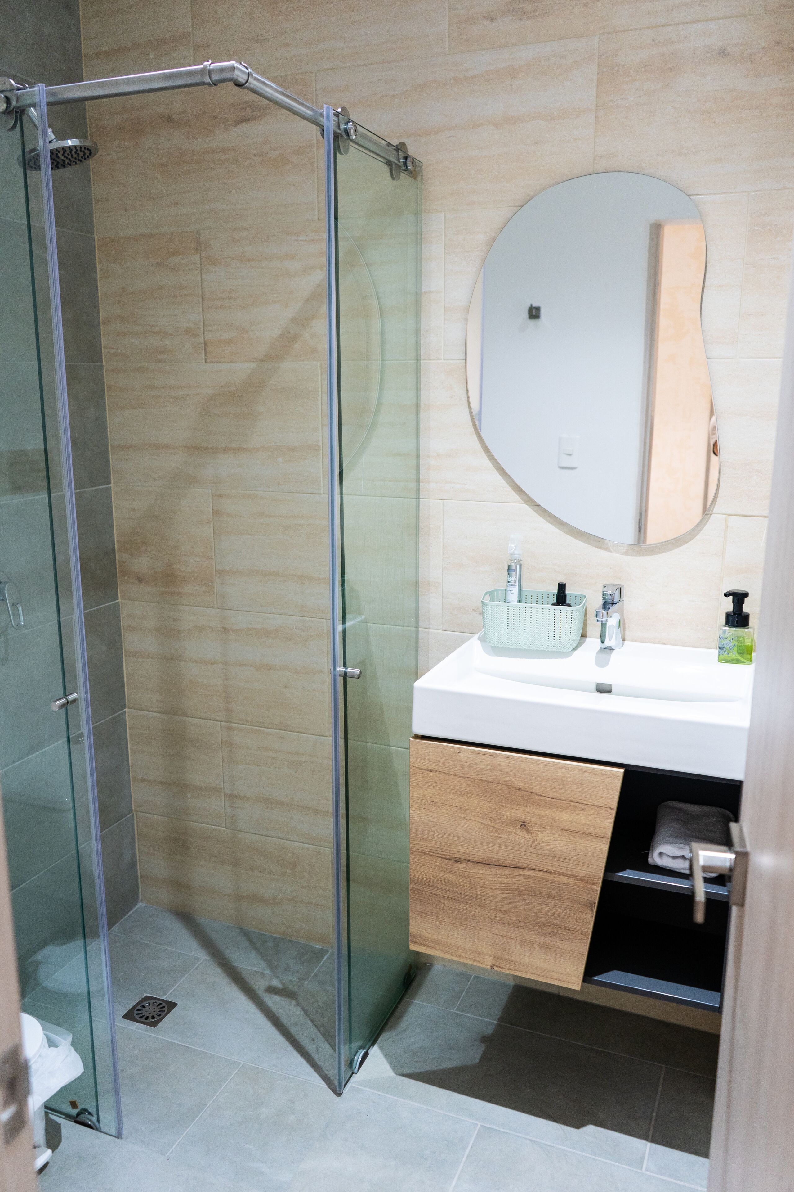 A modern bathroom with a glass-enclosed shower, a wooden vanity with a mirror, and a white sink.