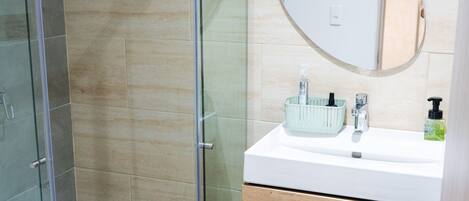 A modern bathroom with a glass-enclosed shower, a wooden vanity with a mirror, and a white sink.
