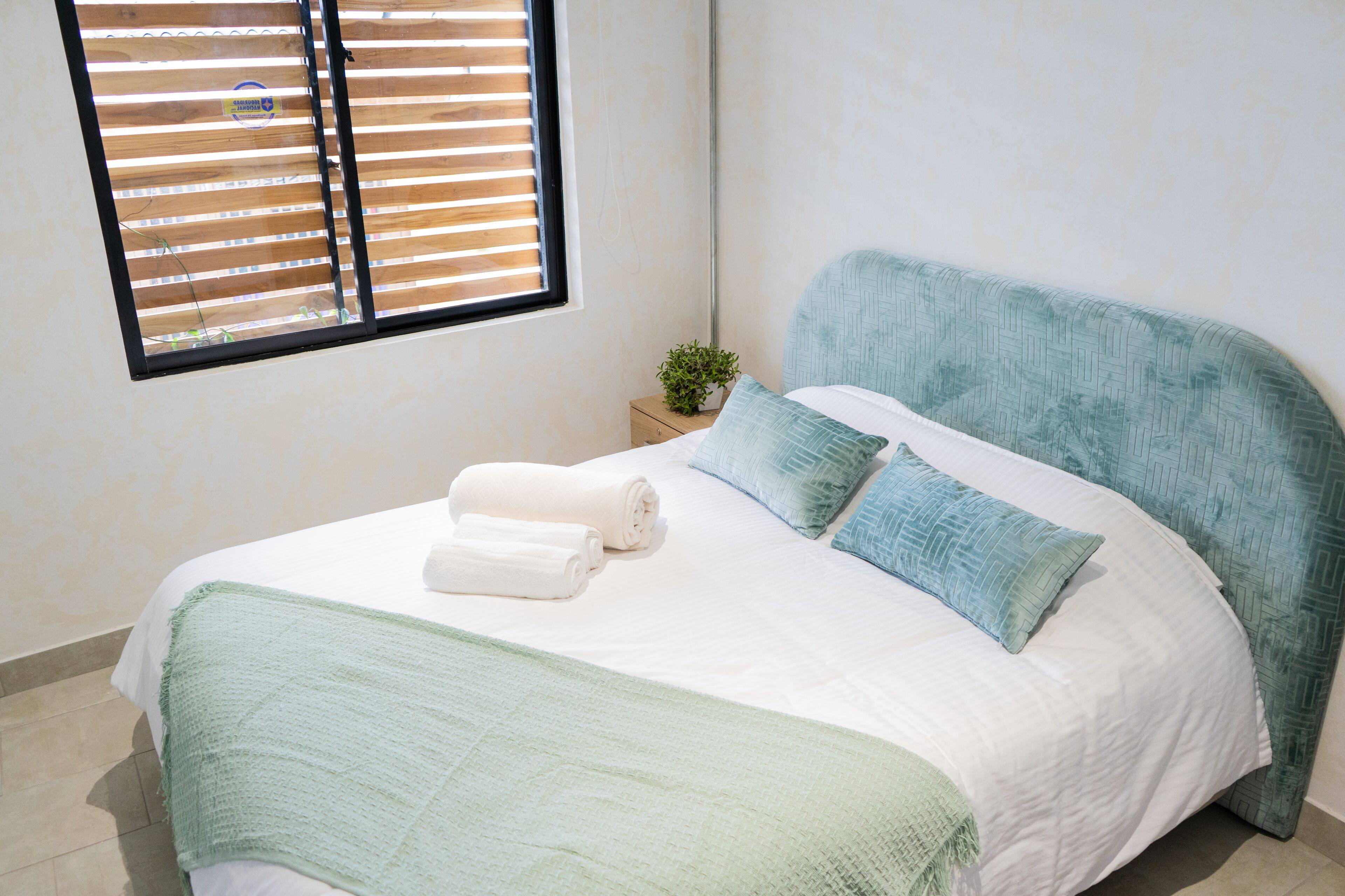 Una cama bien hecha con un edredón verde, dos almohadas y dos toallas enrolladas.