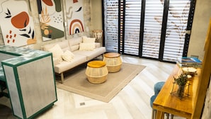 Una sala moderna con un sofá, dos mesas auxiliares redondas de mimbre, una mesa de centro y una mesa de comedor con sillas.