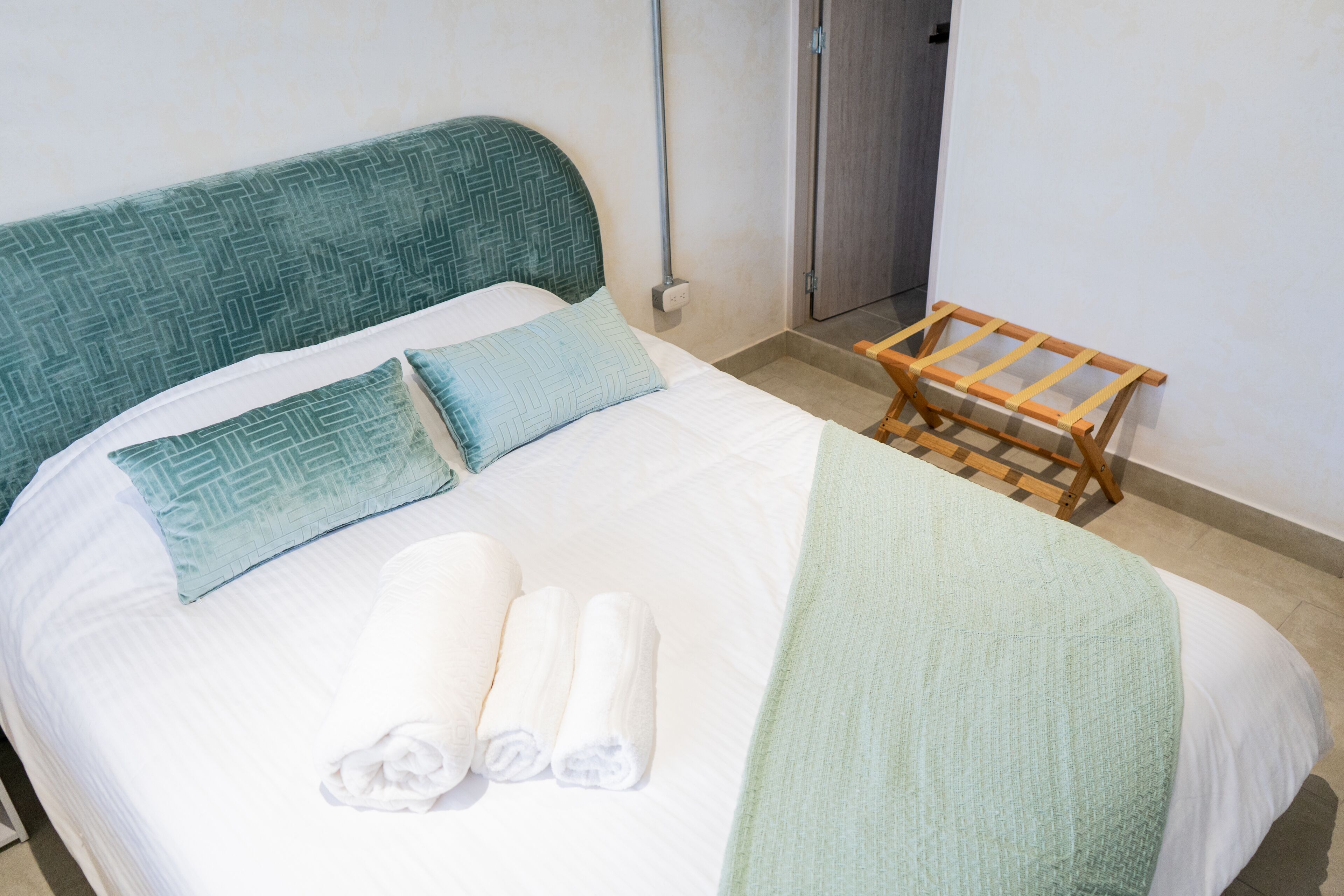 A neatly made bed with pillows, a blanket, and rolled towels.