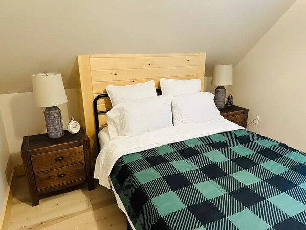 Een slaapkamer met een houten hoofdbord, een bed met witte beddengoed, twee nachtkastjes met lampen en een bedsprei met dessin.