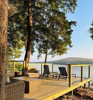 Een houten terras met rieten meubels en stoelen, met uitzicht op een meer.