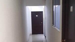 Ein Korridor mit Fliesenboden, einer Tür mit der Aufschrift '01' und einem Fenster an der rechten Wand.
