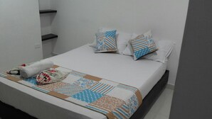 Ein ordentlich bezogenes Bett mit gemusterten Bettwäsche und Kissen, ein aufgerolltes Handtuch und eine kleine Tasche auf dem Bett.