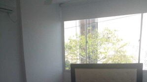 Ein Einzelbett mit Kopfteil, ein Fenster mit Blick auf Bäume und Gebäude sowie ein kleiner Tisch mit einer Tasche darauf.