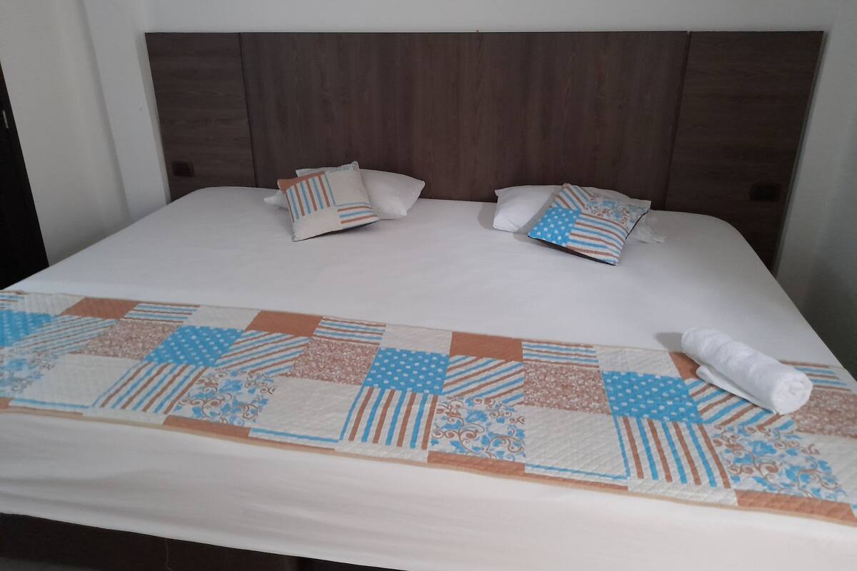 Een netjes opgemaakt bed met een bedsprei met een patroon, twee kussens en een opgerolde handdoek.