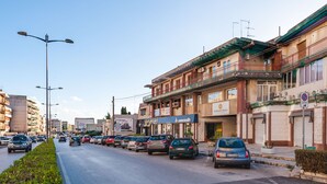 A street with parked cars and buildings, including a hotel with a sign for "Le Cametelle". - Archimede's Rooms (Syracuse)