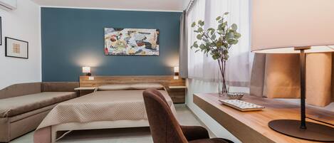 A modern hotel room with a bed, a desk with a lamp, a chair, and a wall-mounted painting.