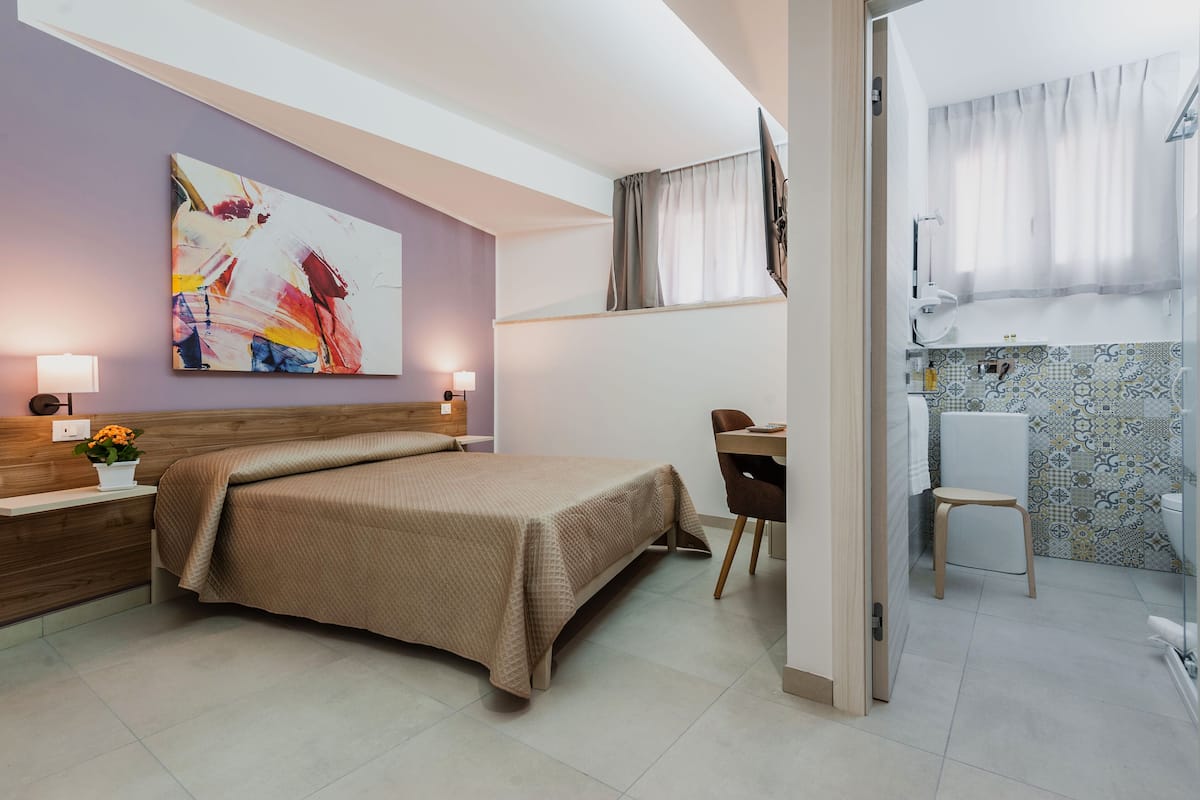A hotel room with a bed, bedside tables, a desk, and a bathroom.