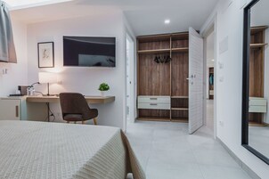 Un dormitorio moderno con cama, escritorio, silla, televisor, armario y una planta pequeña.