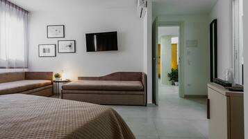 A hotel room with a bed, two sofas, a TV, and framed pictures on the wall.