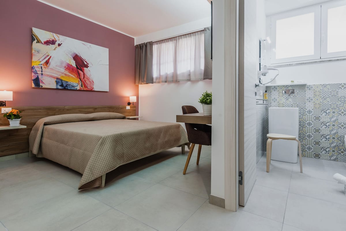 A modern hotel room with a bed, bedside table, lamp, and a large abstract painting on the wall.