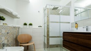 A modern bathroom with a glass shower enclosure, a wooden chair, a white sink, and a vanity with a mirror. - Archimede's Rooms (Syracuse)