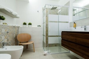 Un baño moderno con cabina de ducha de vidrio, una silla de madera, un lavabo blanco y un mueble de tocador con espejo.