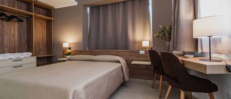 A modern hotel room with a bed, bedside tables, a desk with a chair, a lamp, and a wardrobe.