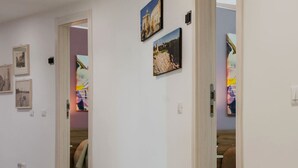 A hallway with white walls, tiled flooring, and several doorways leading to different rooms. - Archimede's Rooms (Syracuse)