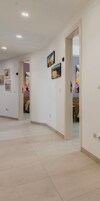 Un pasillo con paredes blancas, suelo de baldosas y varias puertas que dan a diferentes habitaciones.
