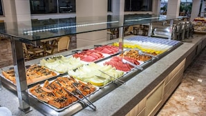 Ein Buffet mit verschiedenen Speisen, darunter Obst, Fleisch und Desserts, hinter einer Glastheke.