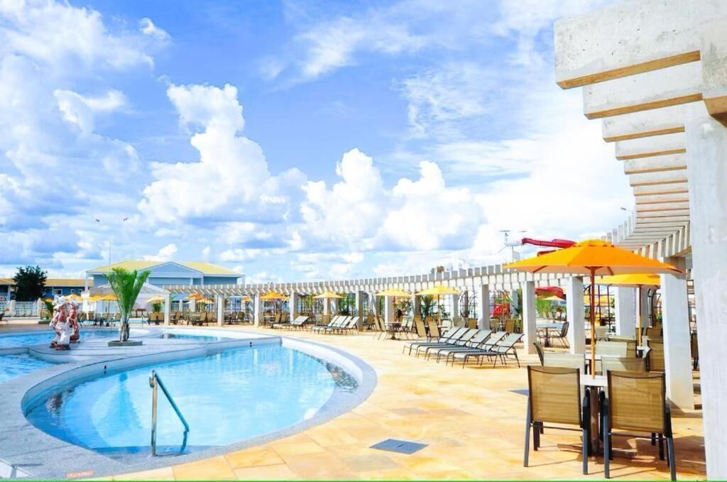 A pool area with lounge chairs and umbrellas, a clear sky, and a building with a white facade.