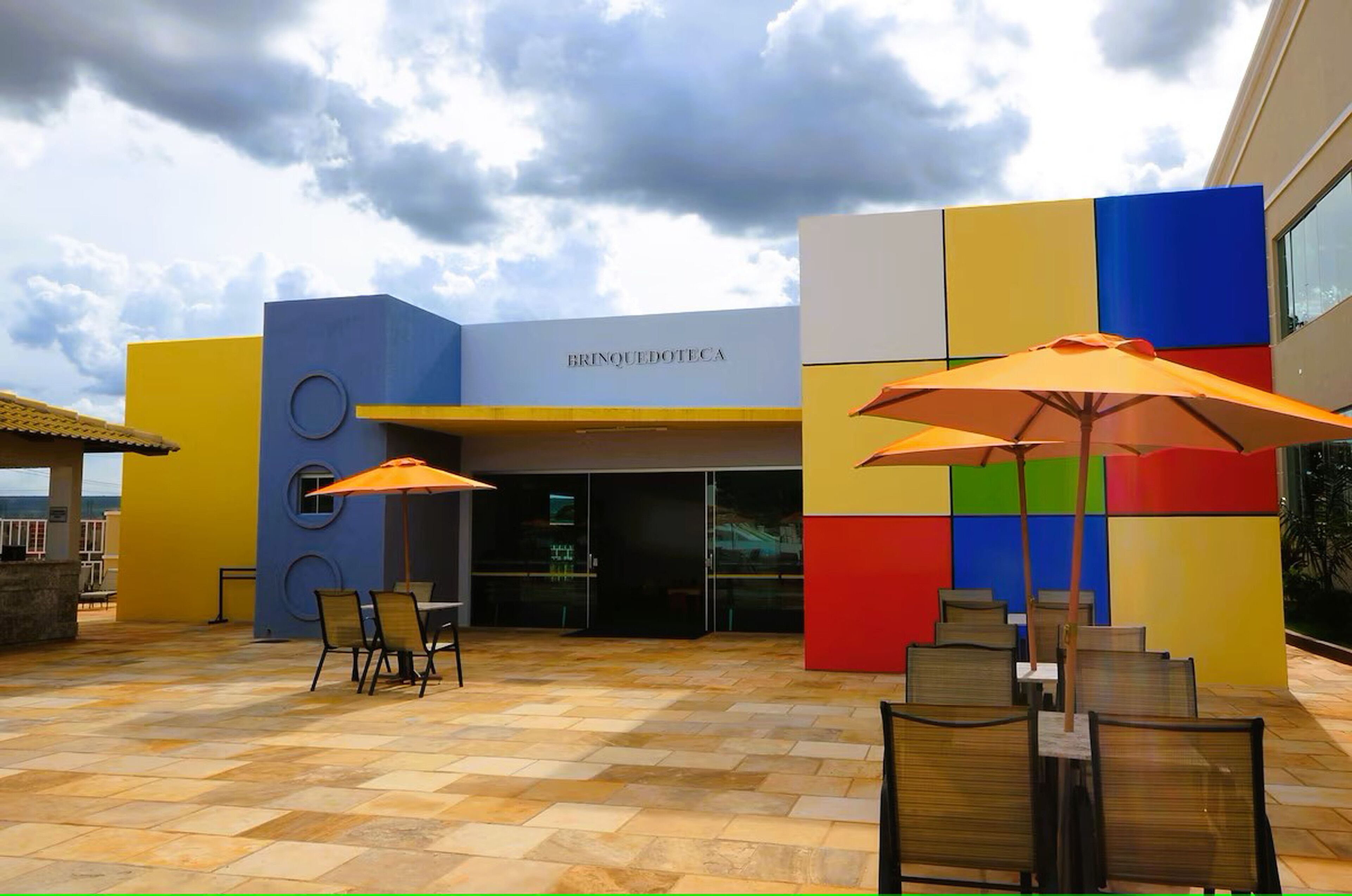 Een modern gebouw met een kleurrijke gevel en een patio met buiten zitplaatsen en parasols.