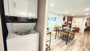 A modern kitchen with a built-in washer and dryer, a dining area with a glass table, and a living room with a sofa and decorative items.