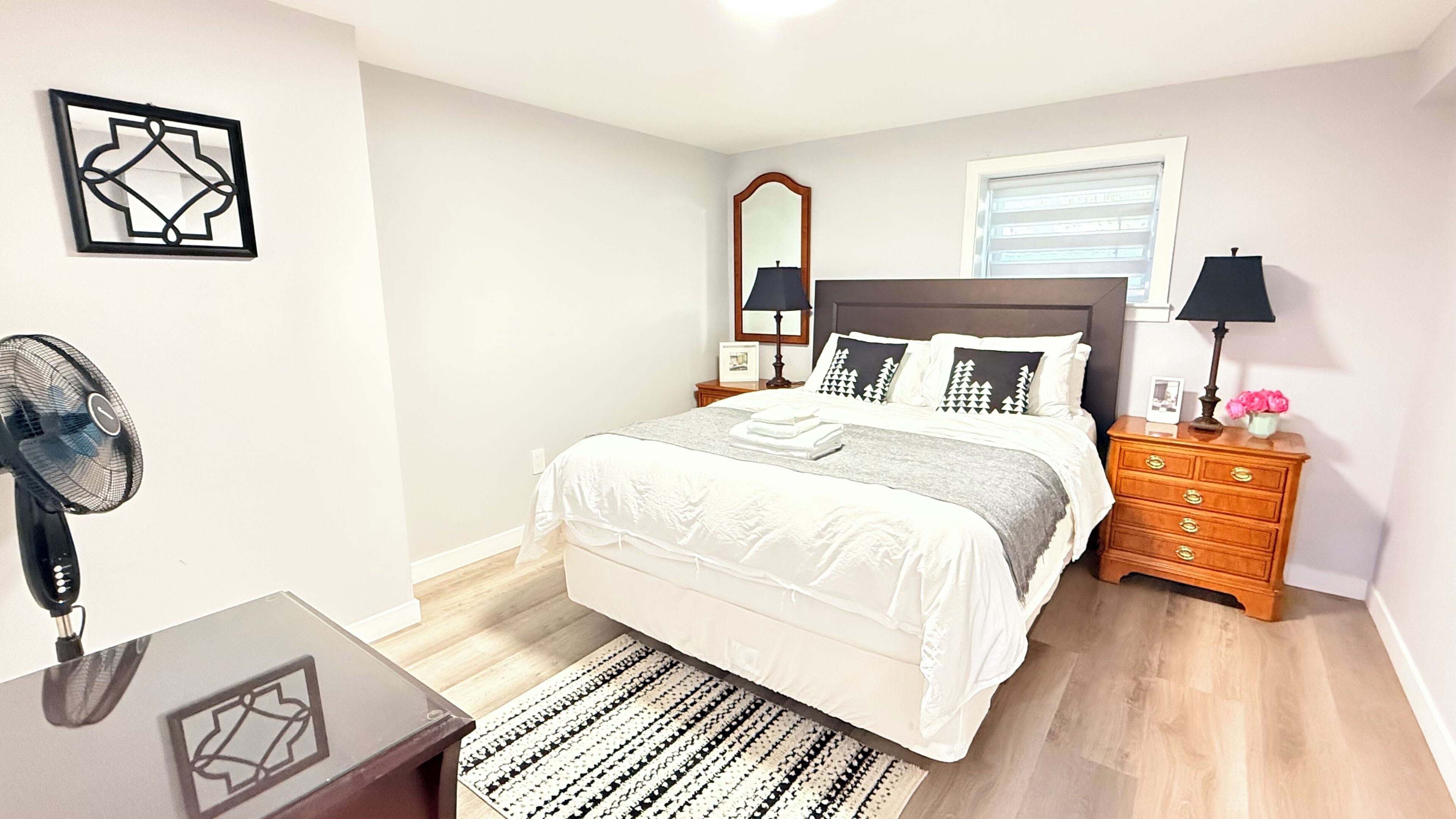 Une chambre à coucher comprenant un lit, des tables de chevet, un miroir, un ventilateur et une commode.