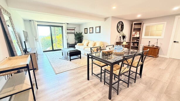 A spacious living area with a dining table, sofa, and a large window with curtains.