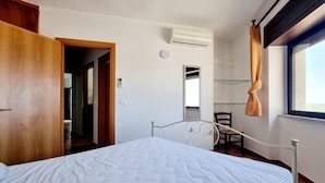 Une chambre à coucher avec un lit, une armoire en bois, une chaise et une fenêtre avec des rideaux.
