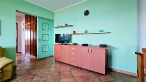 Un salon avec un téléviseur, un meuble rose, des murs verts et un sol carrelé.