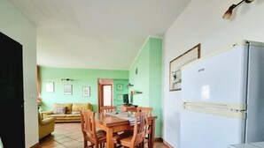 Un coin repas avec une table et des chaises en bois, un réfrigérateur blanc et un mur vert orné de tableaux.