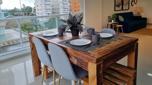 Comedor con mesa de madera dispuesta para cuatro, balcón con vistas a edificios y sala de estar con sofá y objetos decorativos.