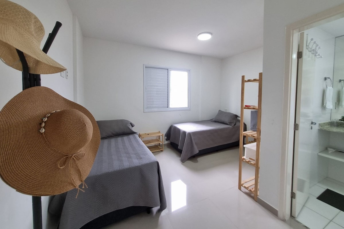 A small, clean room with two single beds, a window, and a shower area.