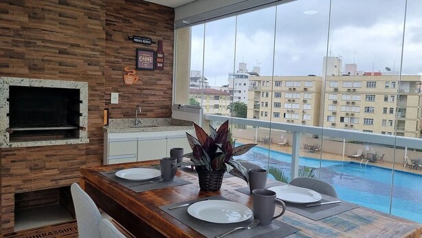 Comedor con mesa de madera, sillas y vista a una piscina y edificios.